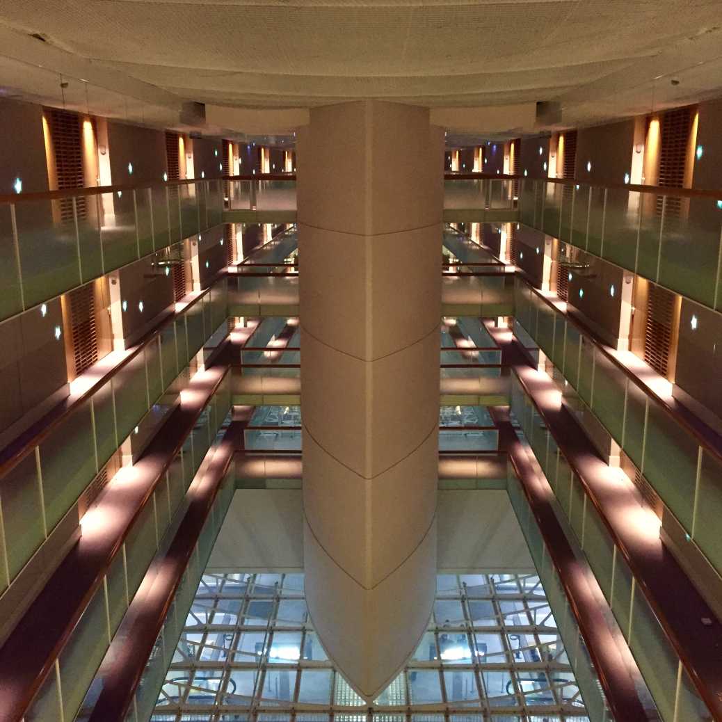 Vue intérieure d'un atrium à plusieurs étages avec balcons et éclairage chaleureux, tons dorés et ambiance feutrée, grain argentique visible.